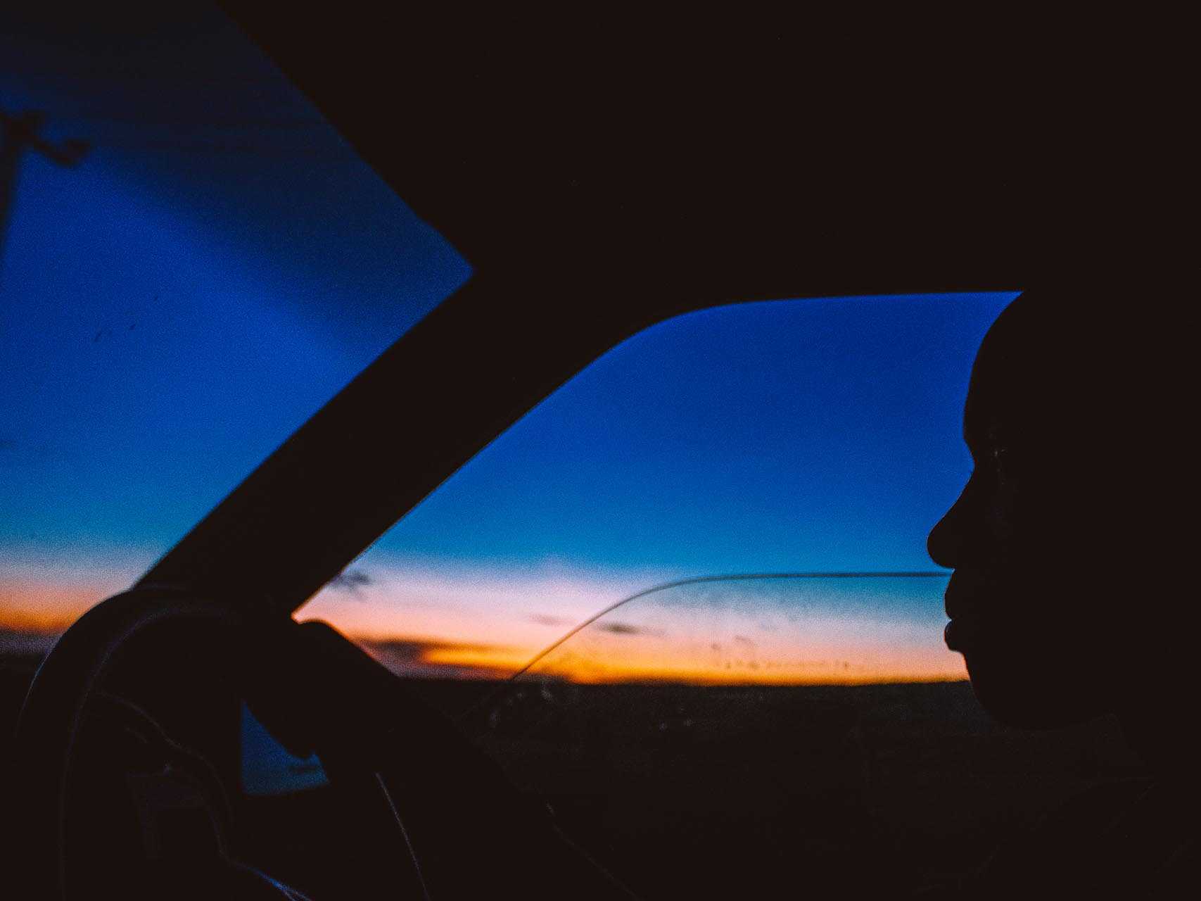 A driver in a car driving in the blue hour after sunset.